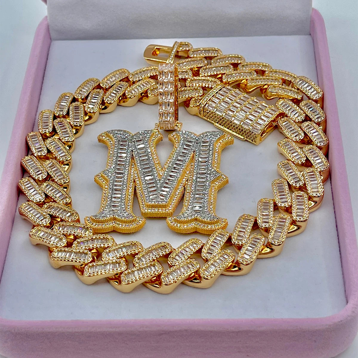 Gold chain necklace with a large letter 'M' pendant on a pink cushioned base.