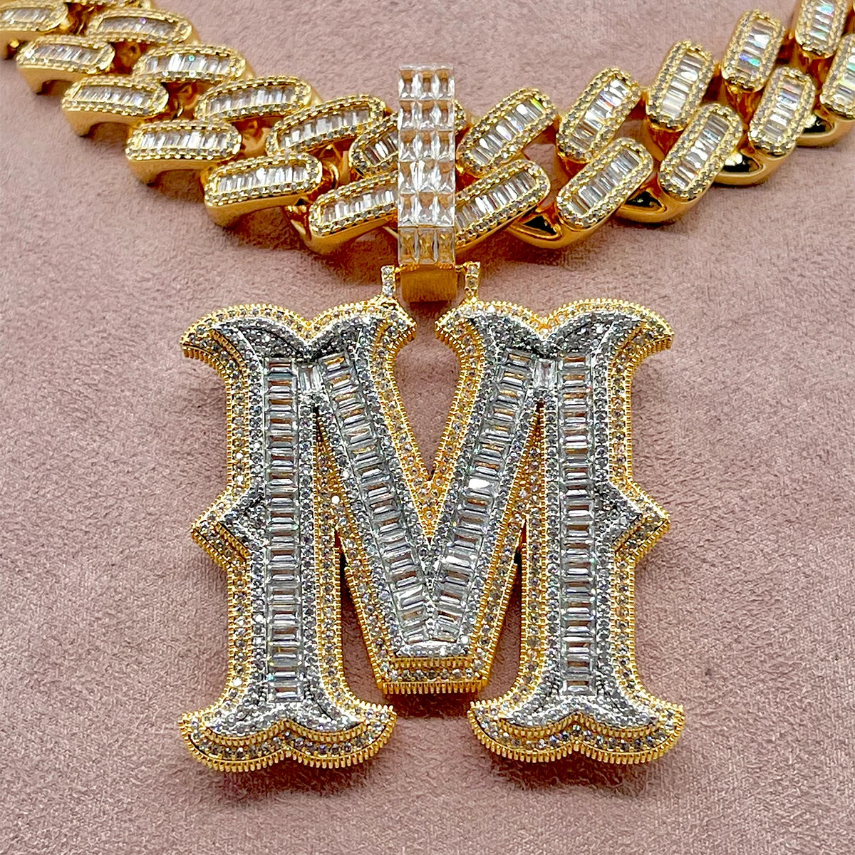 Gold and silver letter 'M' pendant on a pink background