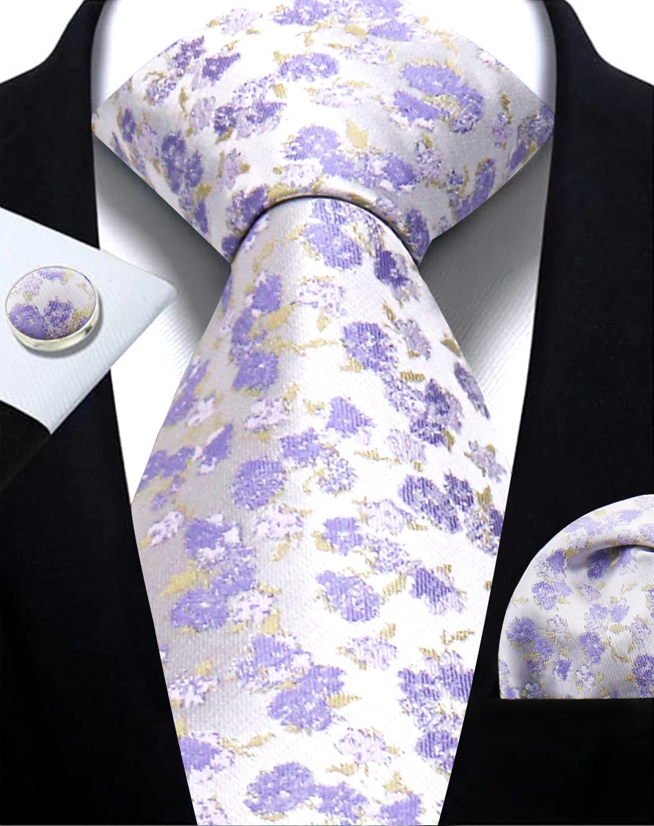 Set of purple floral tie, pocket square, cufflinks, and handkerchief on a black suit.